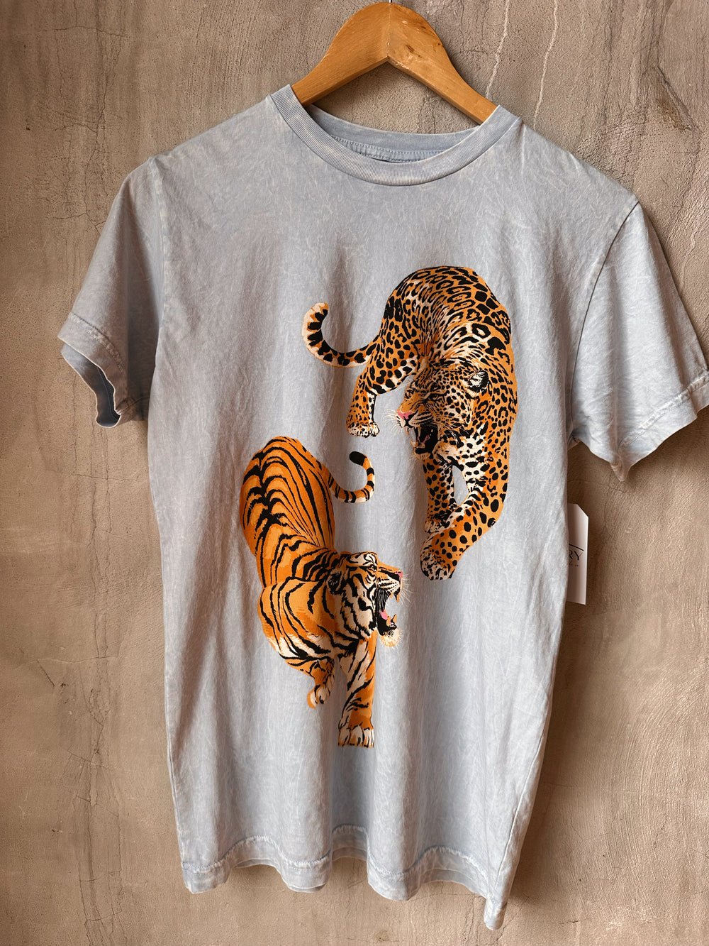 Gray t-shirt with a graphic of a tiger and a leopard on a wooden surface.