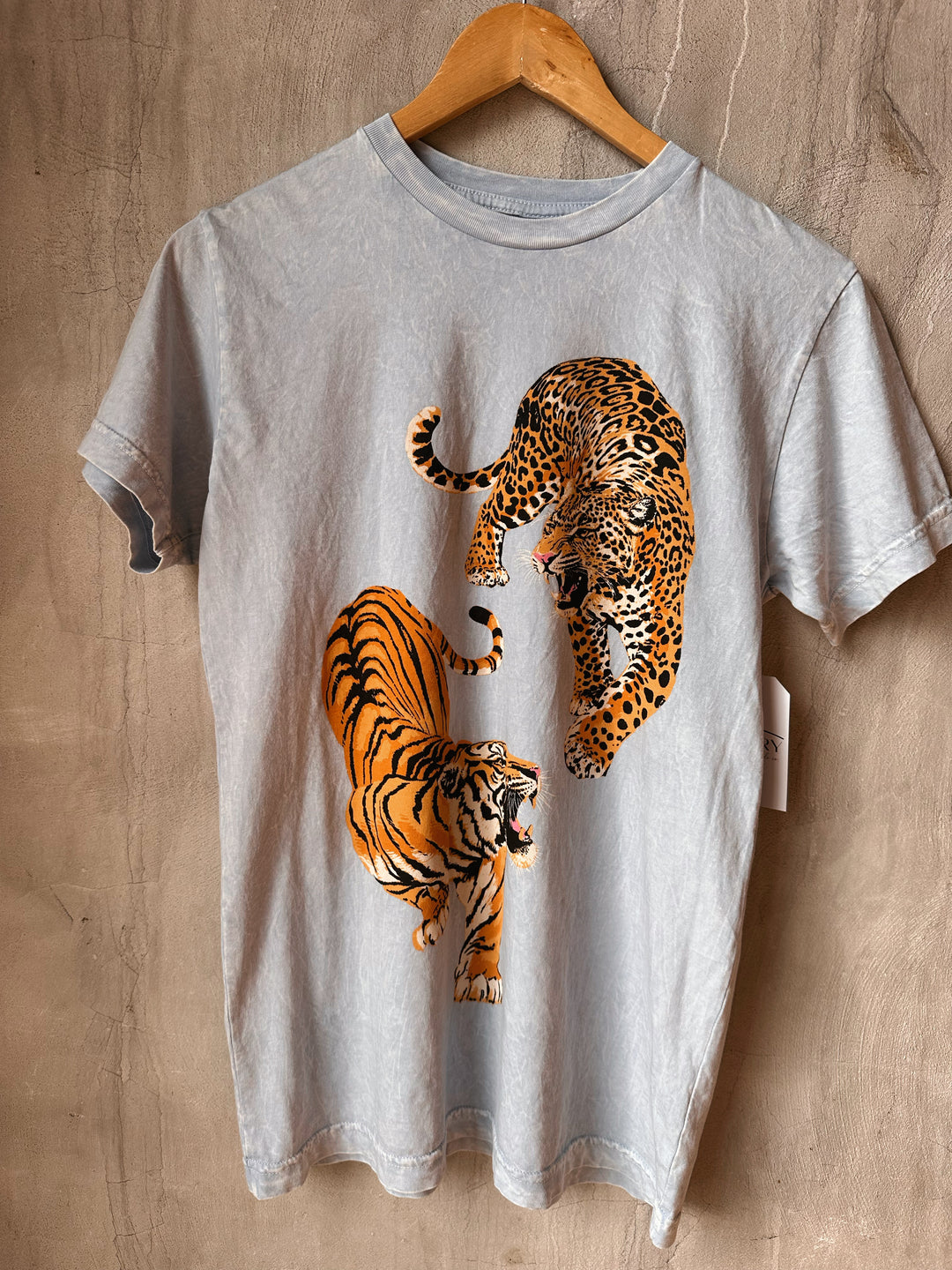 Gray t-shirt with a graphic of a tiger and a leopard on a wooden surface.