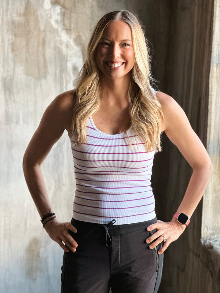 Woman wearing a striped tank top and dark pants against a textured wall.