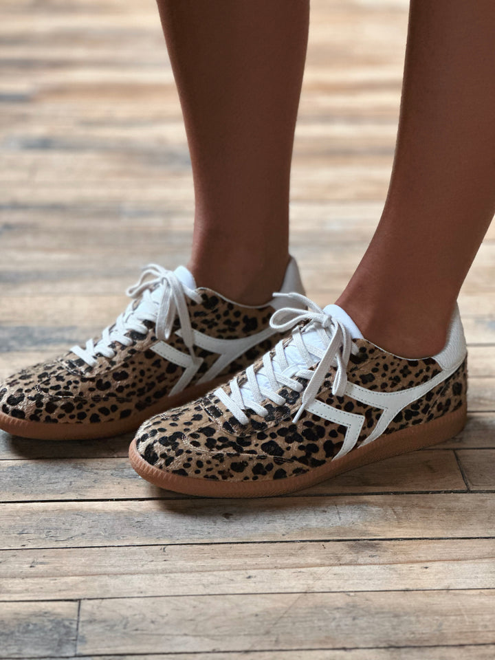 Leopard print sneakers with white laces on a wooden floor.