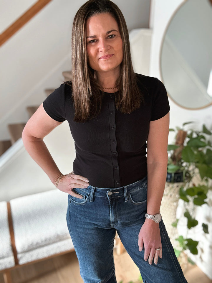 Woman in black top and jeans standing in a home interior.