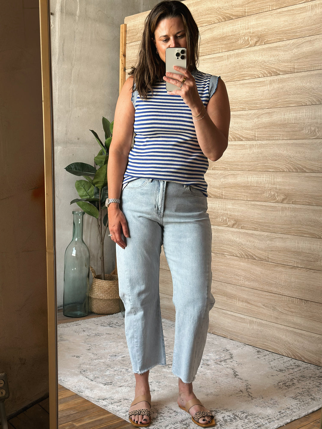 Woman wearing a blue and white striped tank top and light blue jeans in a room with wooden walls and decor.