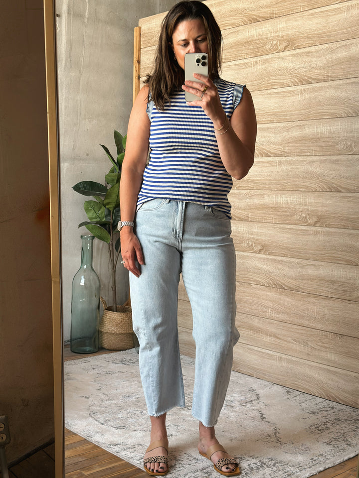 Woman wearing a blue and white striped tank top and light blue jeans in a room with wooden walls and decor.
