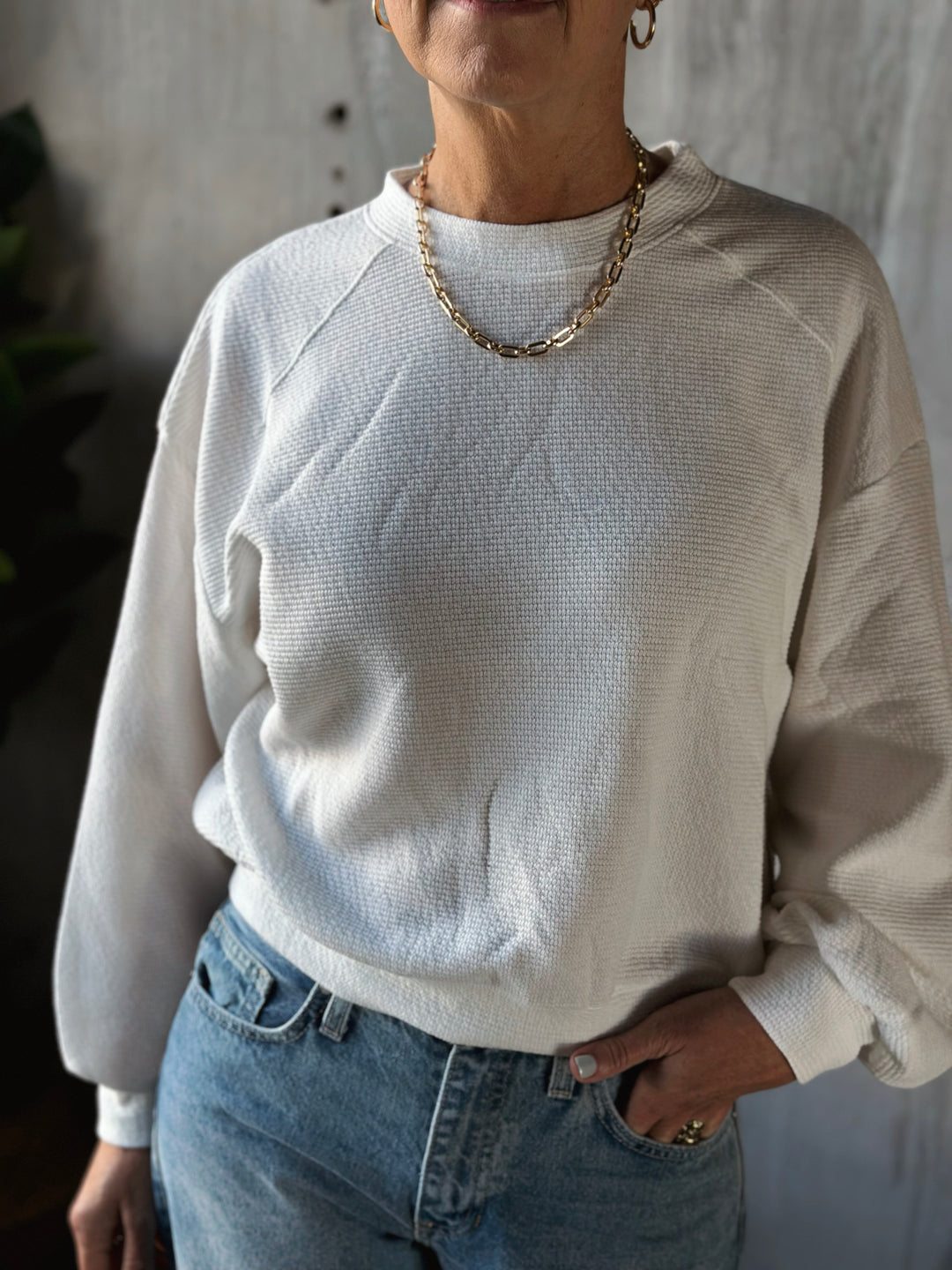 Person wearing a light-colored sweater and blue jeans with a neutral background