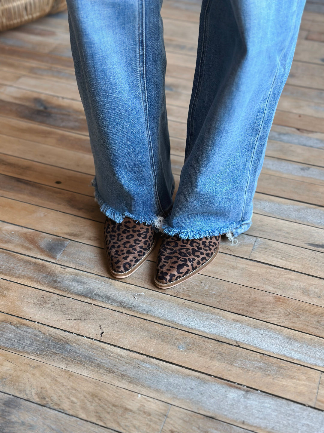 Person wearing blue jeans and leopard print shoes on a wooden floor