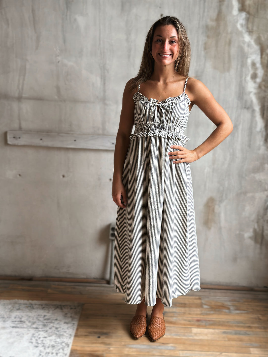 Woman wearing a white and gray striped dress standing in a room with a concrete wall.