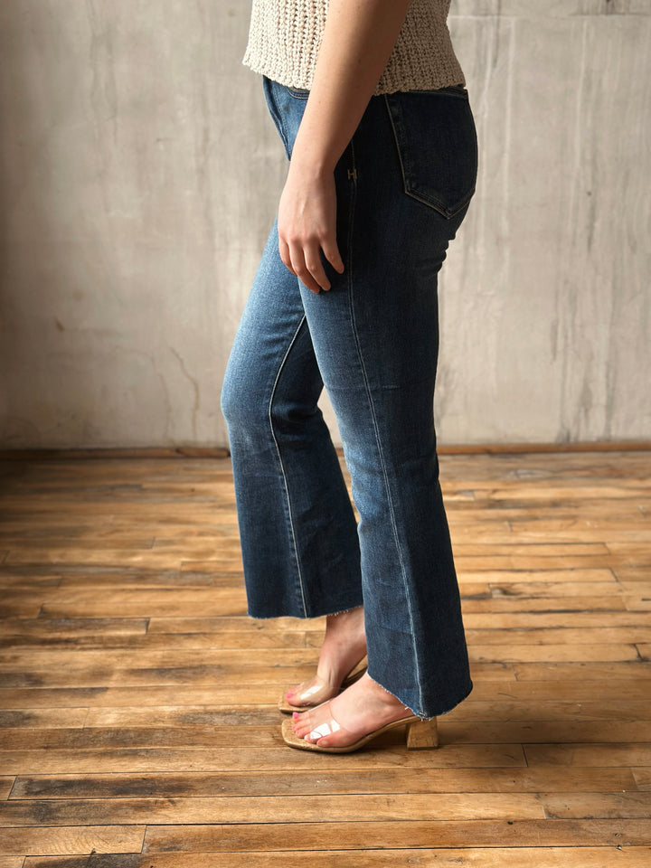 Person wearing blue jeans standing on a wooden floor with a neutral wall background