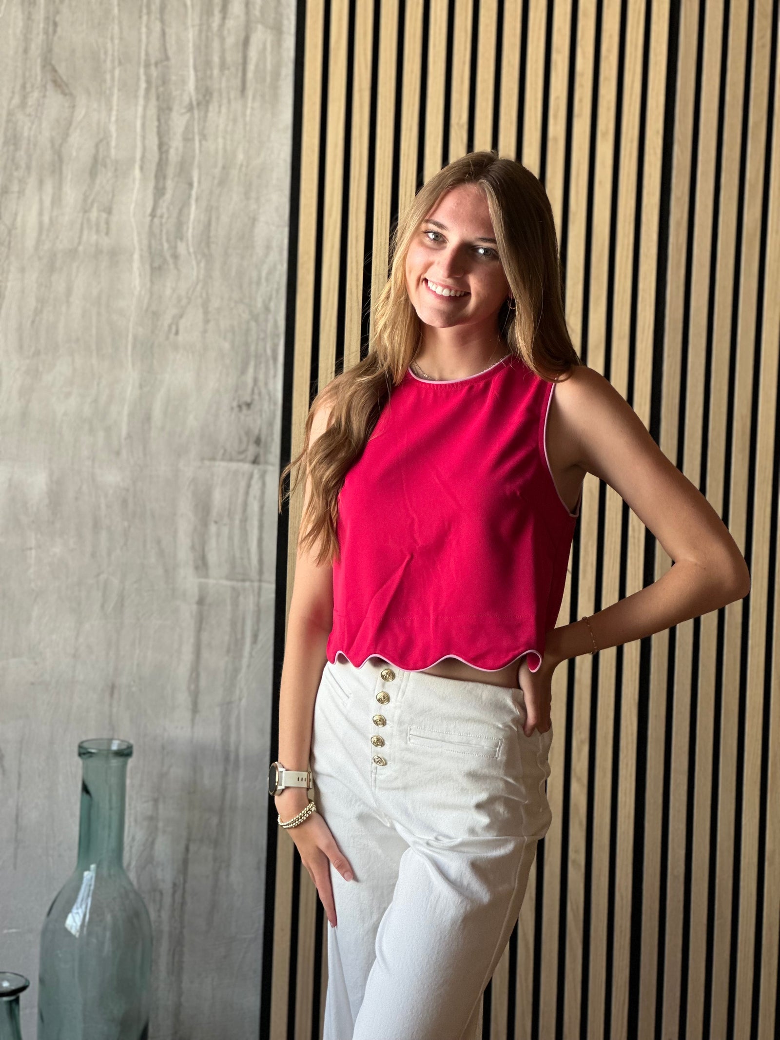Front view of model wearing a scarlet colored top with a sleeveless design and scalloped hem and a button closure on the back of top