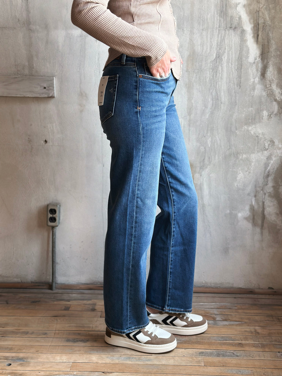 Person wearing blue jeans and a beige sweater in a room with a concrete wall.