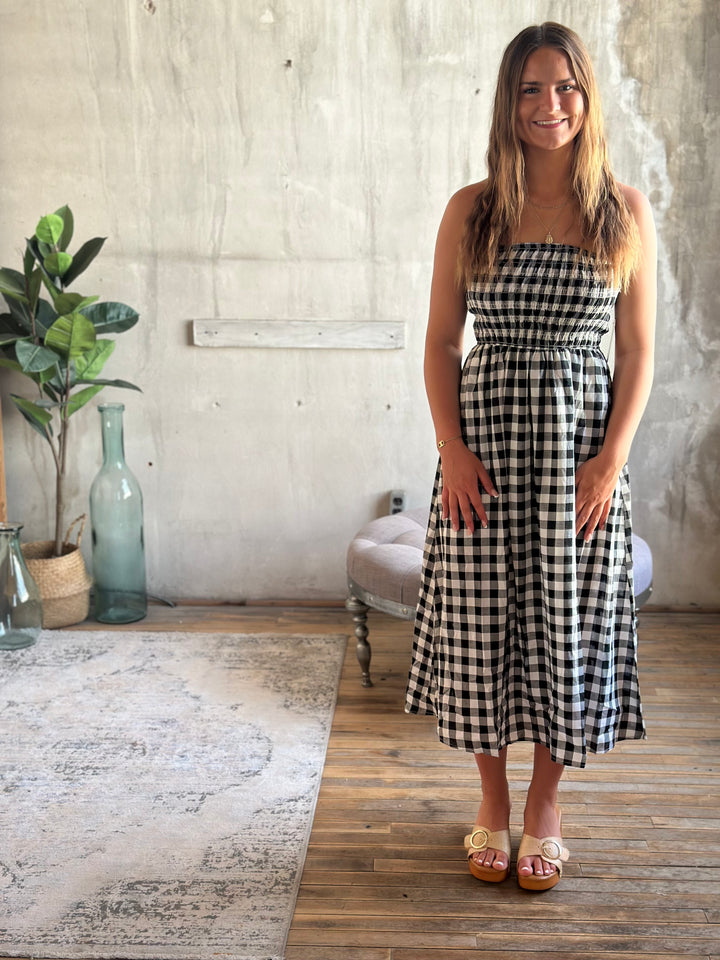 Woman in a black and white plaid strapless dress standing in a room with a plant and a rug.