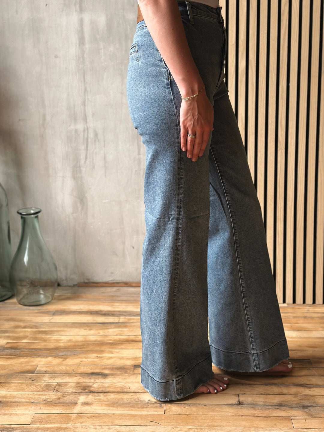 Person wearing wide-leg jeans standing on a wooden floor with a neutral background