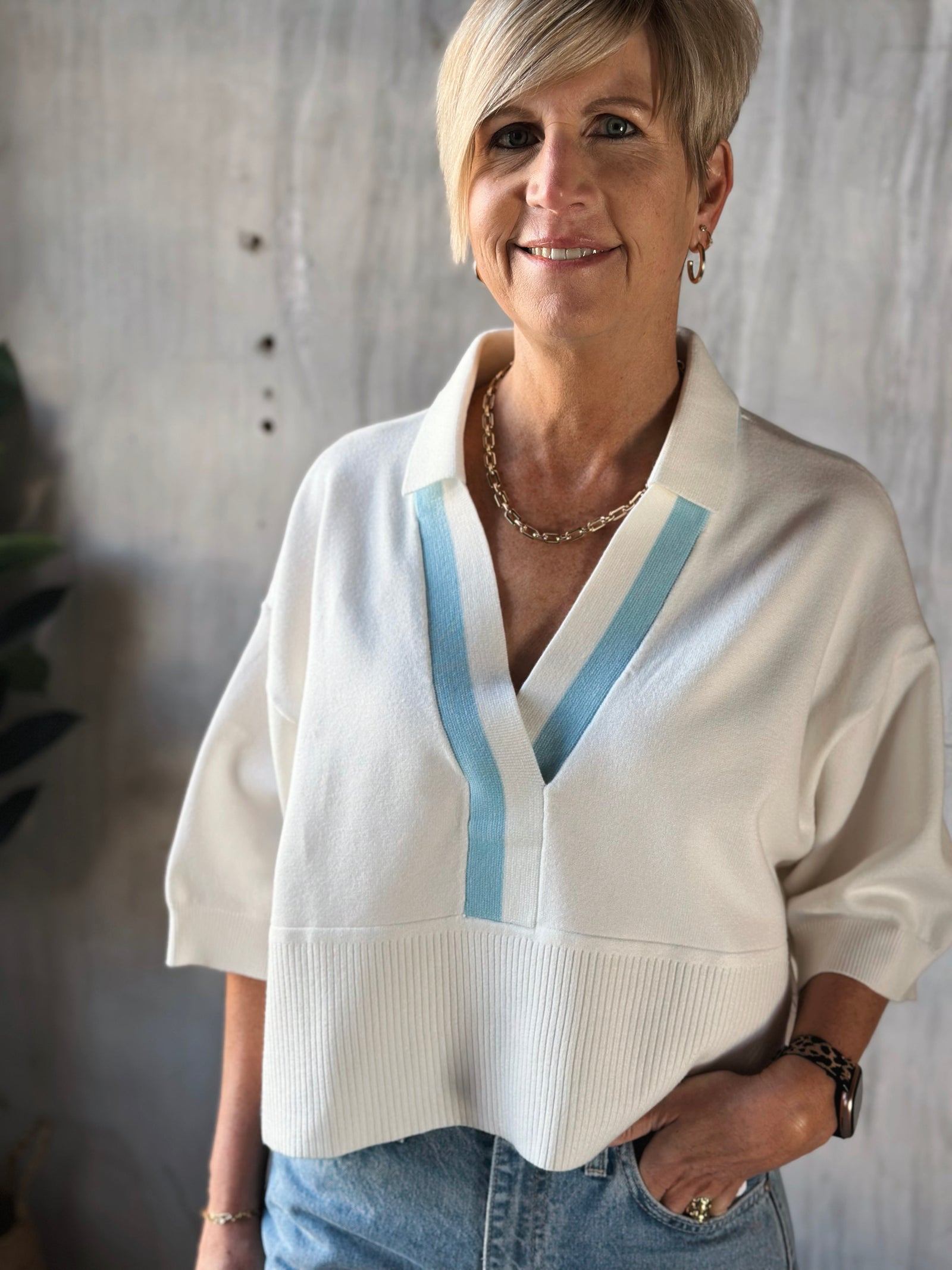 Woman wearing a white sweater with blue accents against a neutral background