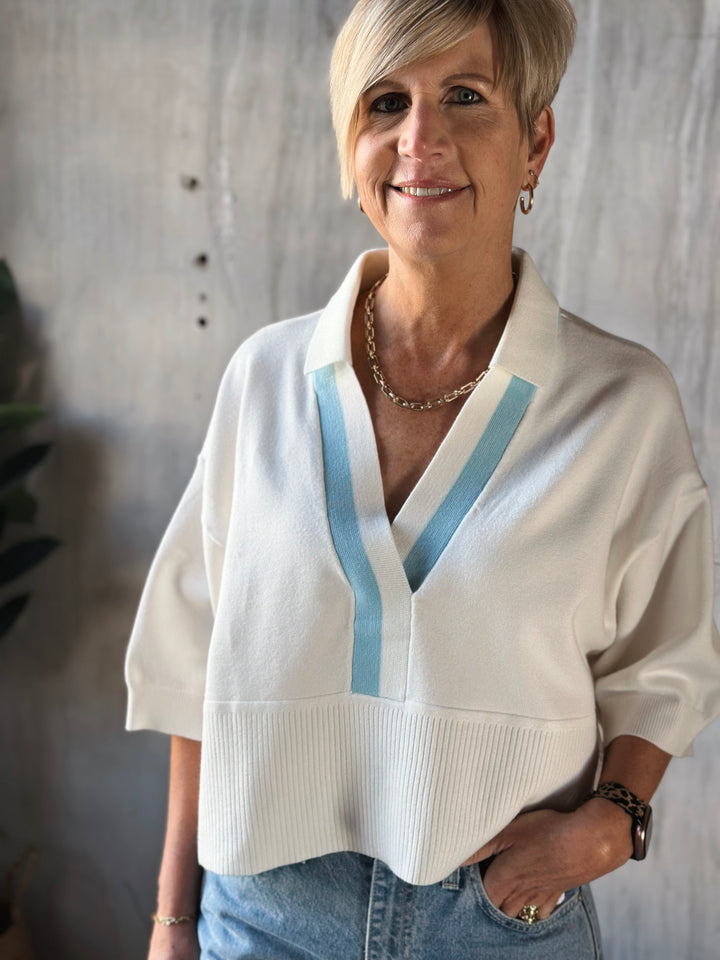 Woman wearing a white sweater with blue accents against a neutral background