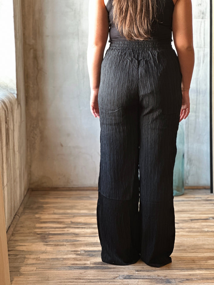 Person wearing black pants standing in a room with wooden floor and light-colored walls.