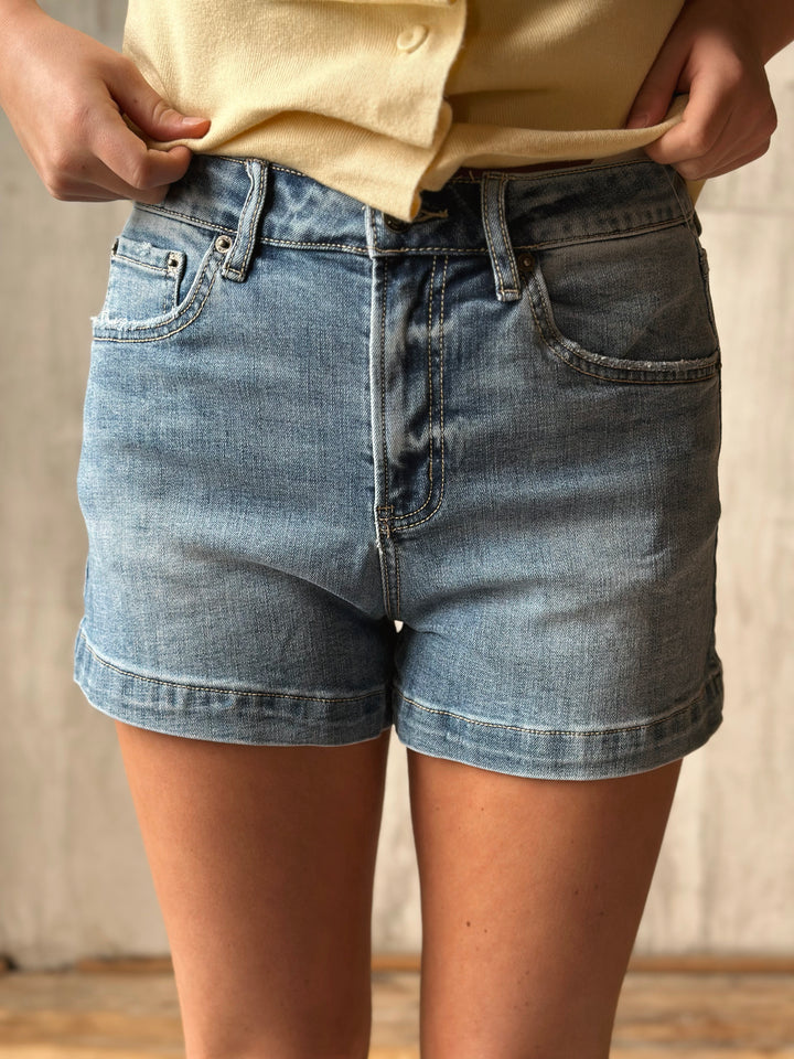 Person wearing light blue denim shorts with a neutral background
