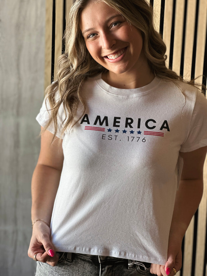 Front picture of model wearing America EST 1776 Crop Top in white with navy and red writing