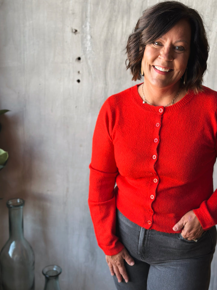 Woman wearing a red sweater standing against a concrete wall with decorative bottles.