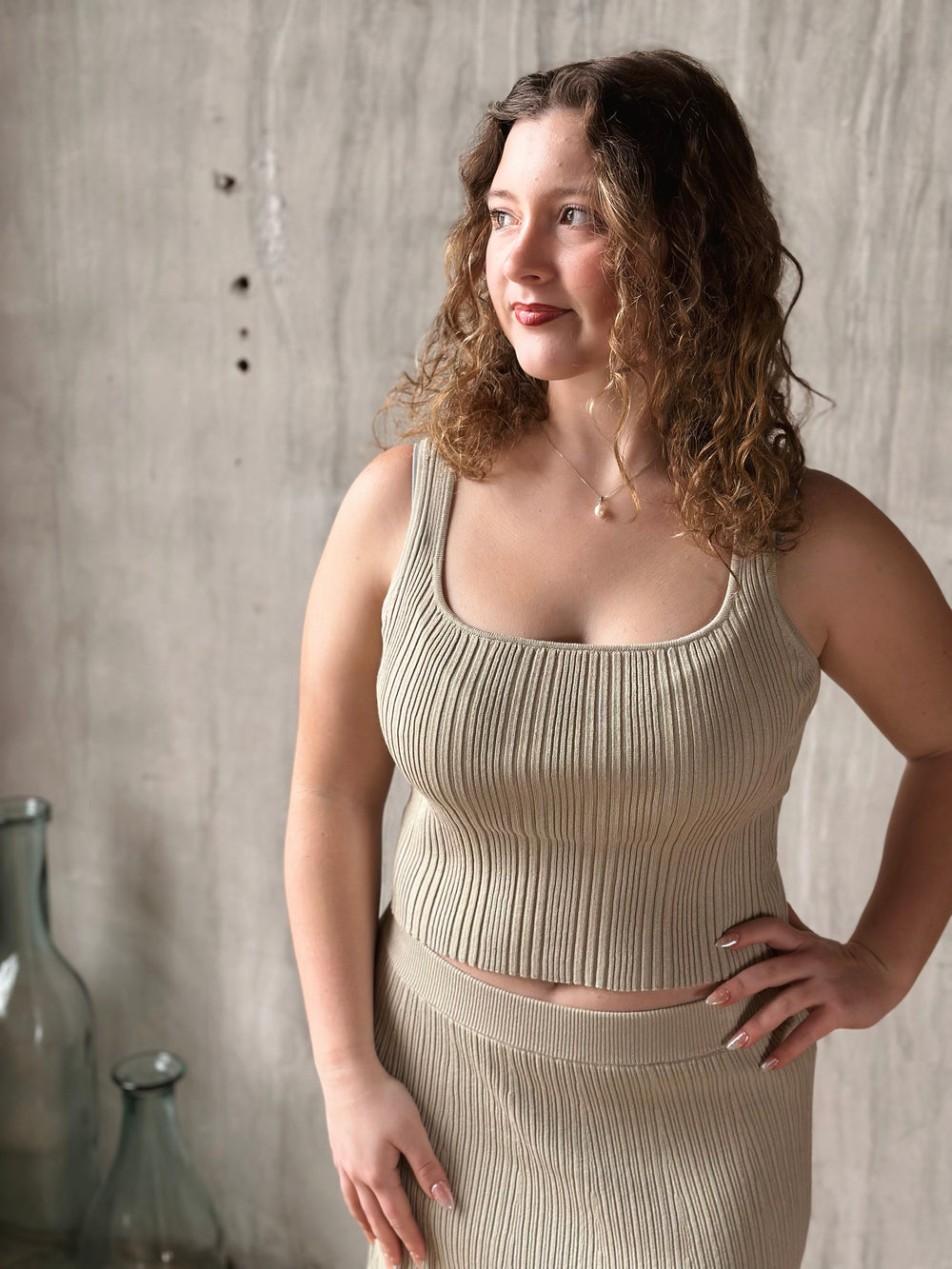 Woman wearing a beige ribbed top and skirt against a textured wall.