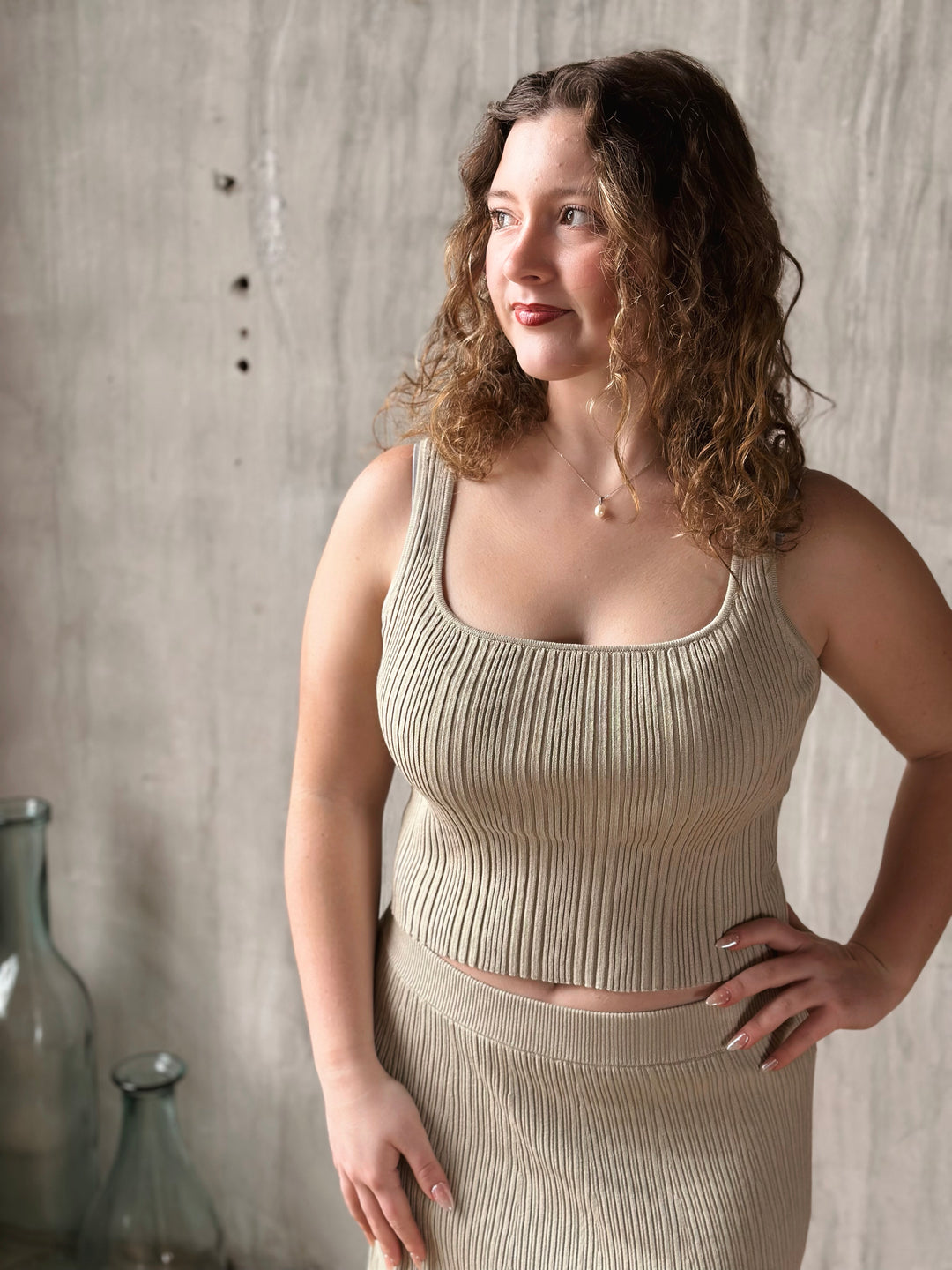 Woman wearing a beige ribbed top and skirt against a textured wall.