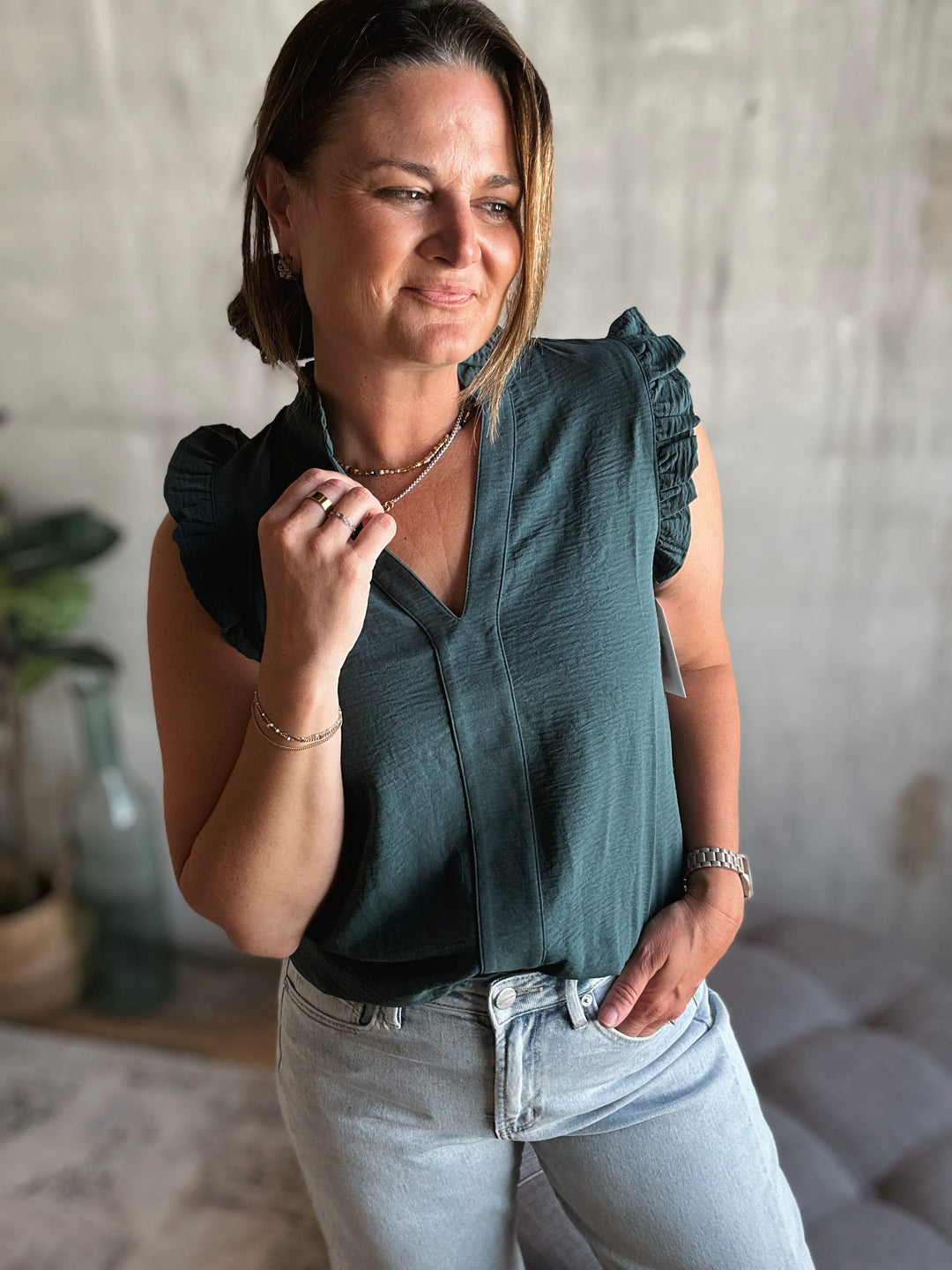 Woman wearing a dark green v-neck blouse with ruffled sleeves in an indoor setting.