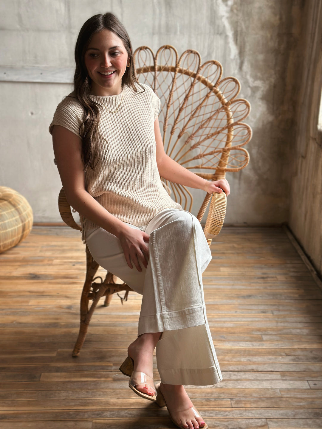 Woman sitting on a wicker chair wearing a beige outfit in a warm-toned room.
