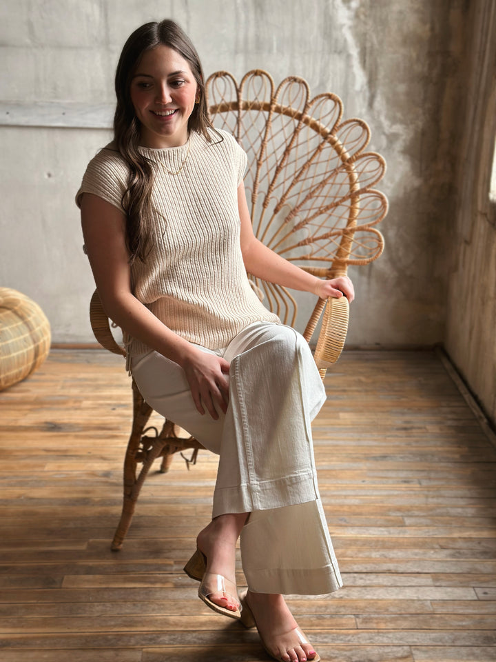 Woman sitting on a wicker chair wearing a beige outfit in a warm-toned room.