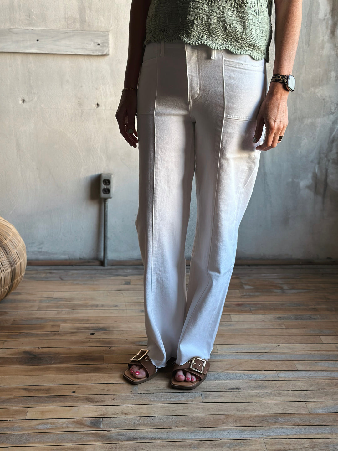 Person wearing light-colored pants and sandals in a room with wooden flooring and a textured wall.