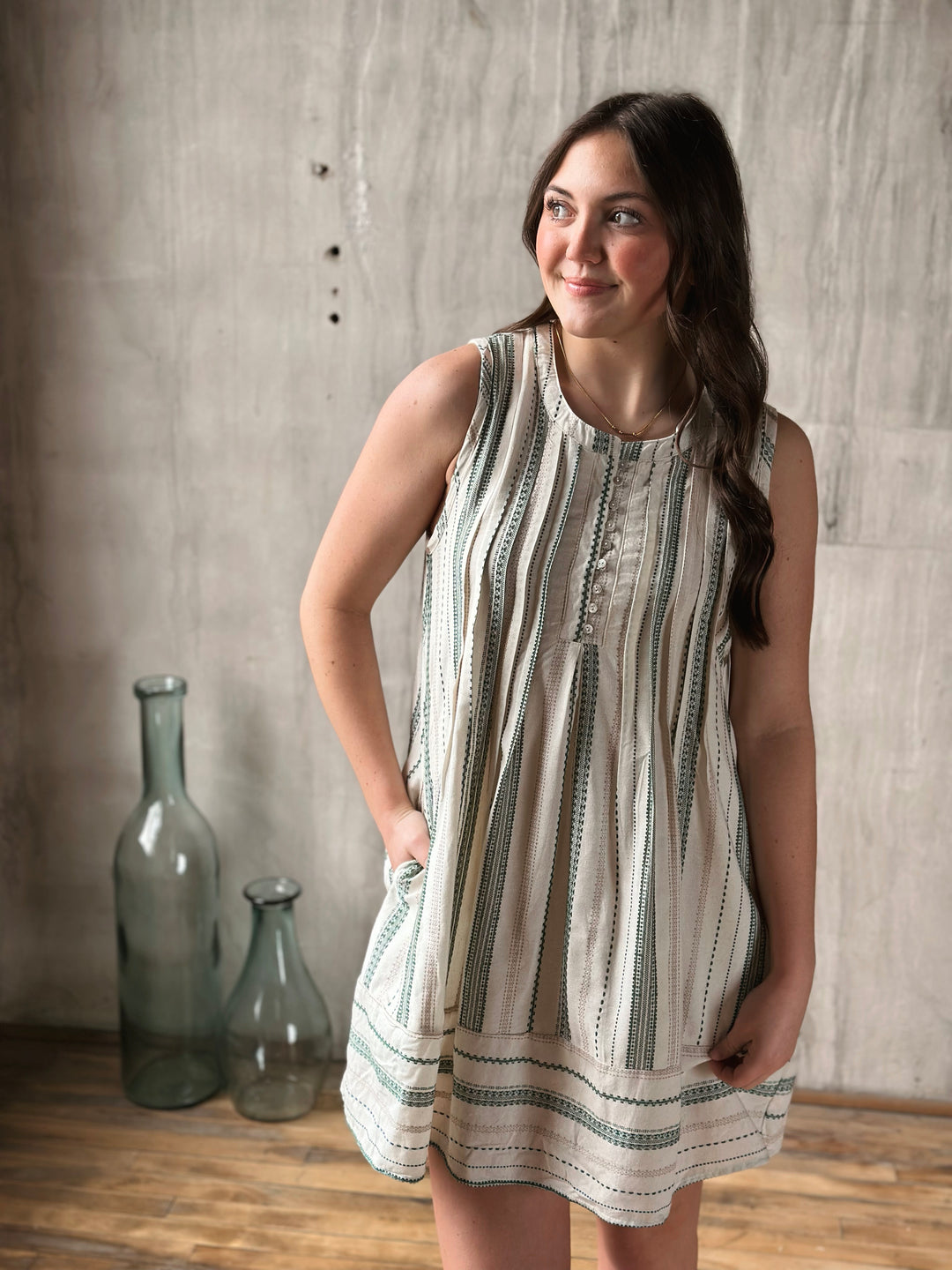 Woman wearing a sleeveless dress with a pattern, standing against a wooden wall.