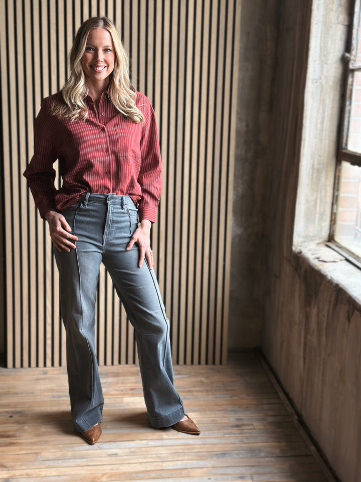 Woman wearing a red sweater and blue jeans standing in a room with wooden floor and striped wall.