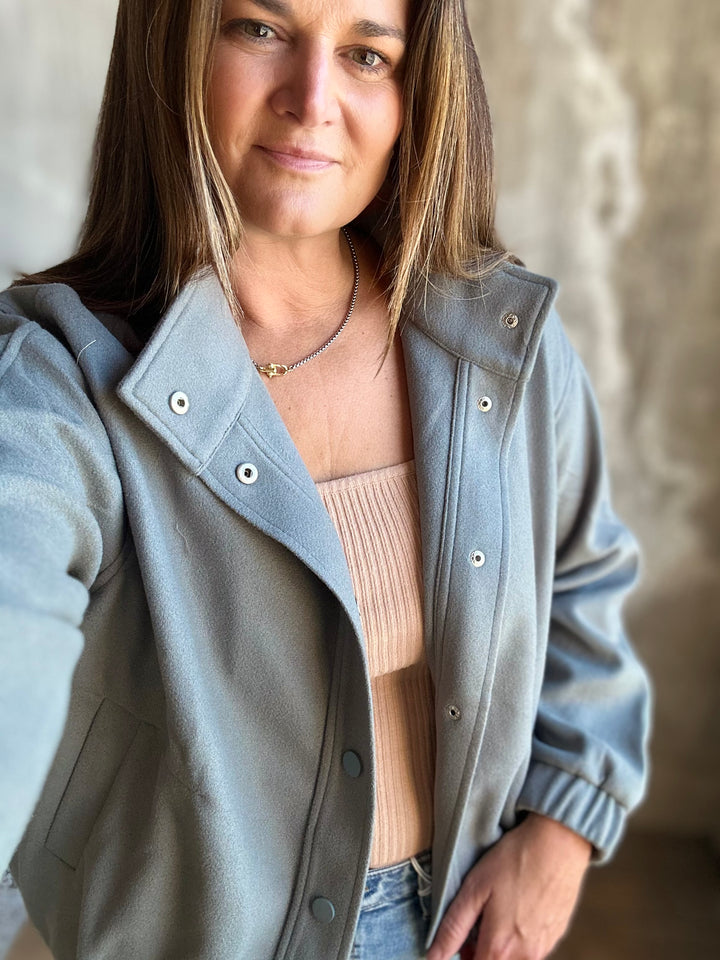 Woman wearing a slate blue snap-front jacket with a stand collar over a tan top