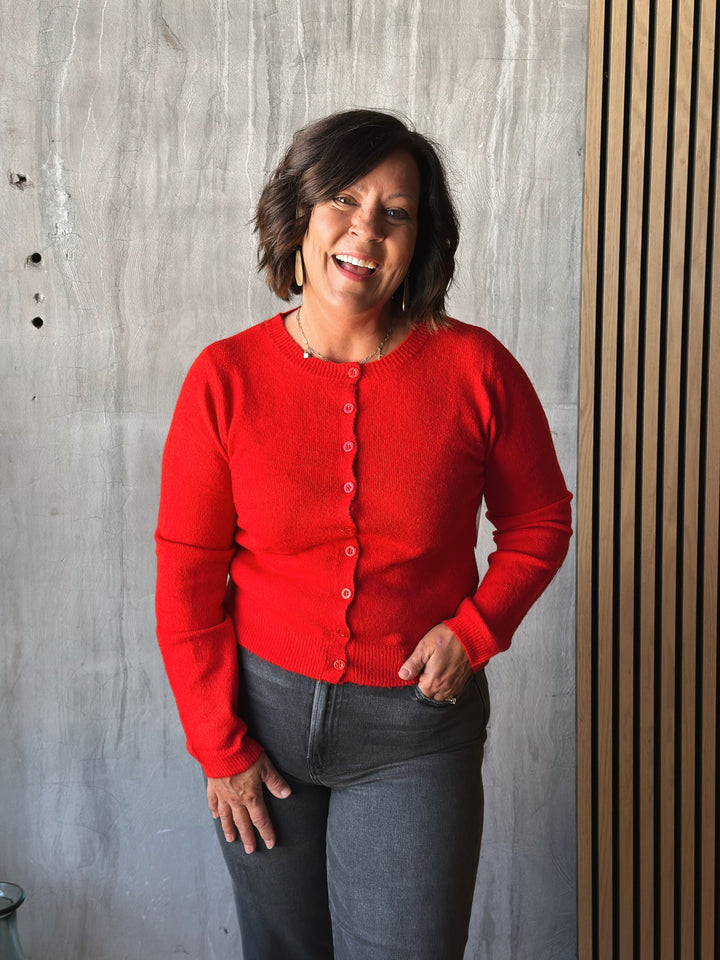 Person wearing a red cardigan standing against a textured wall.