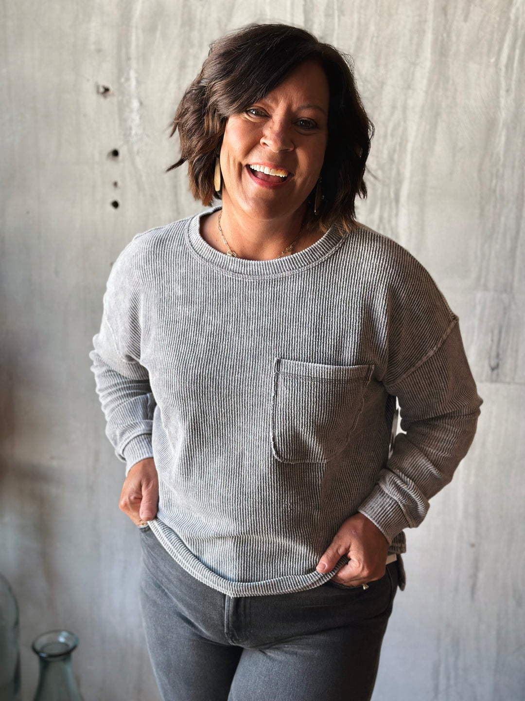 Woman wearing a gray sweater with a pocket against a textured wall.