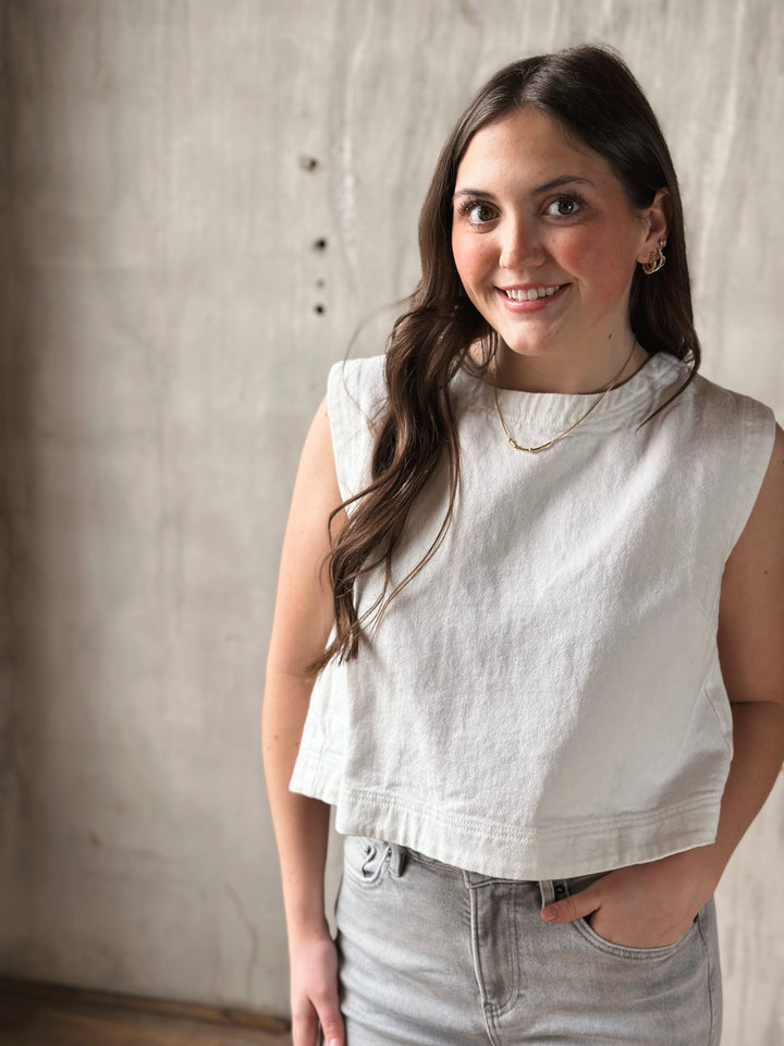 Woman wearing a white denim sleeveless top and gray pants against a neutral background