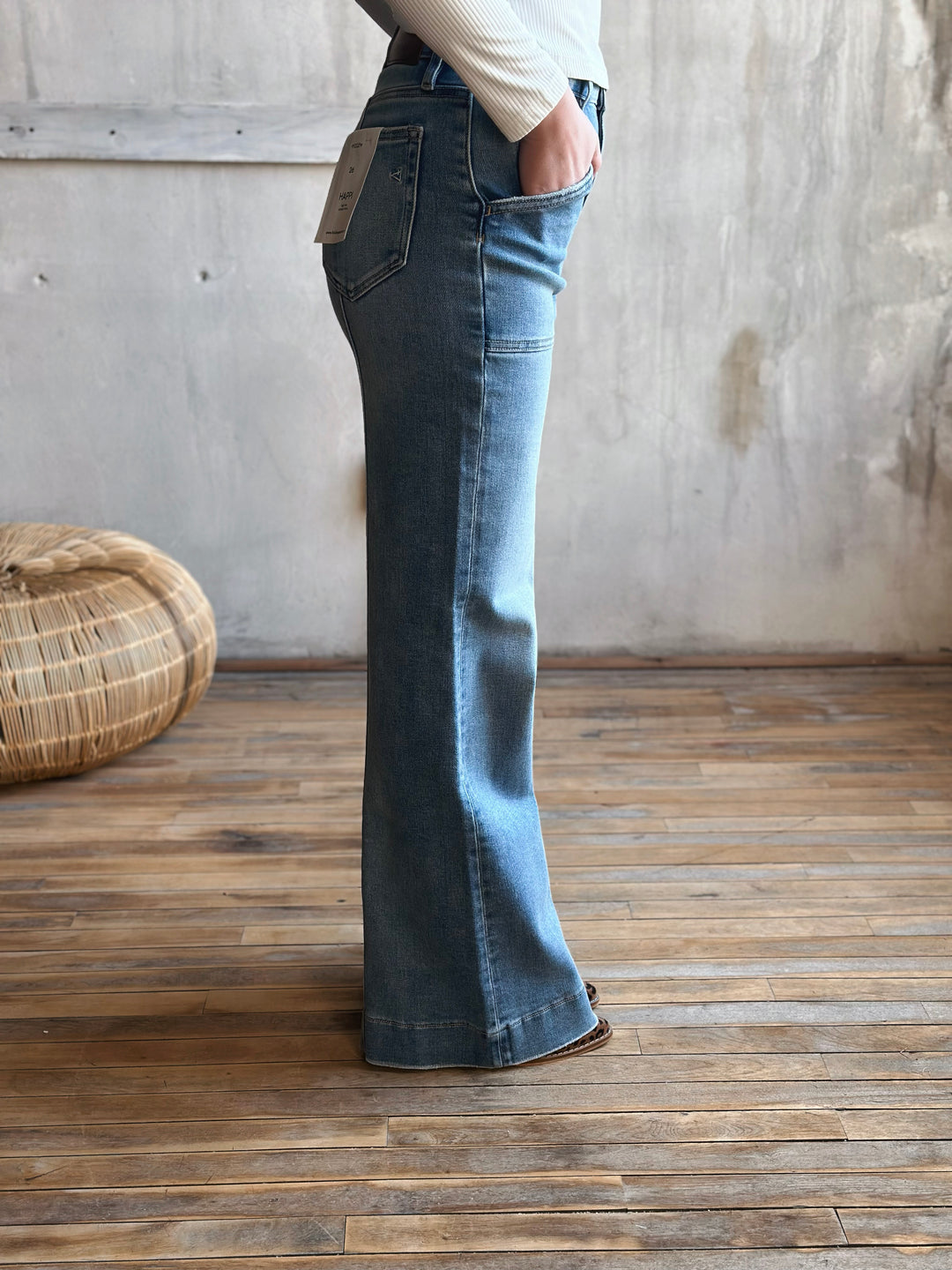 Person wearing blue flared jeans standing in a room with wooden flooring and a woven basket.