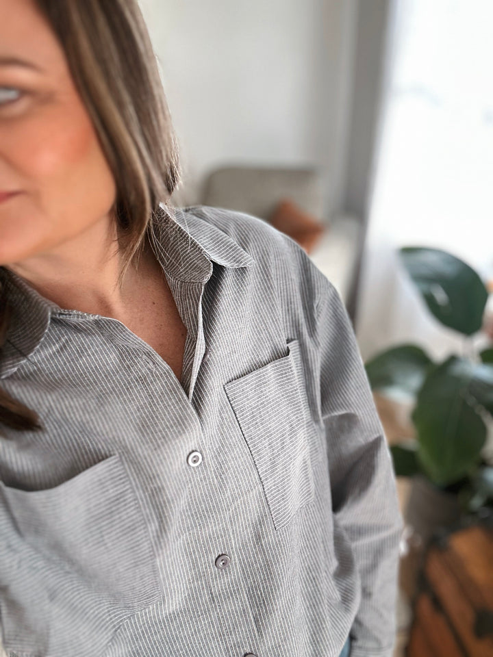 Person wearing a gray button-up shirt indoors with a blurred background