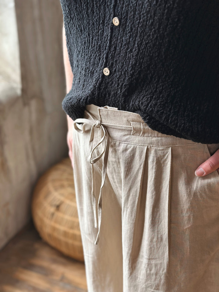 A person wearing a dark textured sweater and beige pants with strings in a softly lit room.