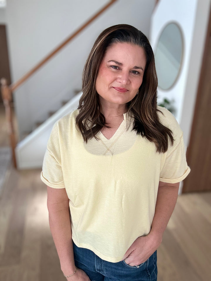 Woman wearing a light yellow shirt and blue jeans indoors.