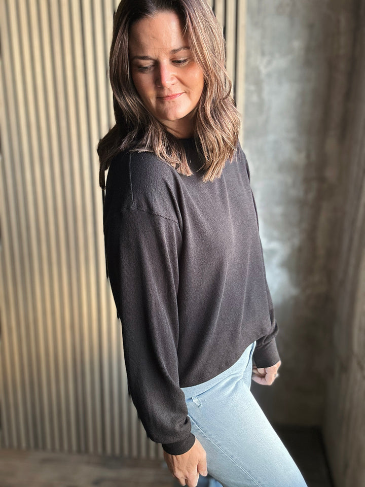 Woman wearing a dark gray sweater and light blue jeans against a textured wall.