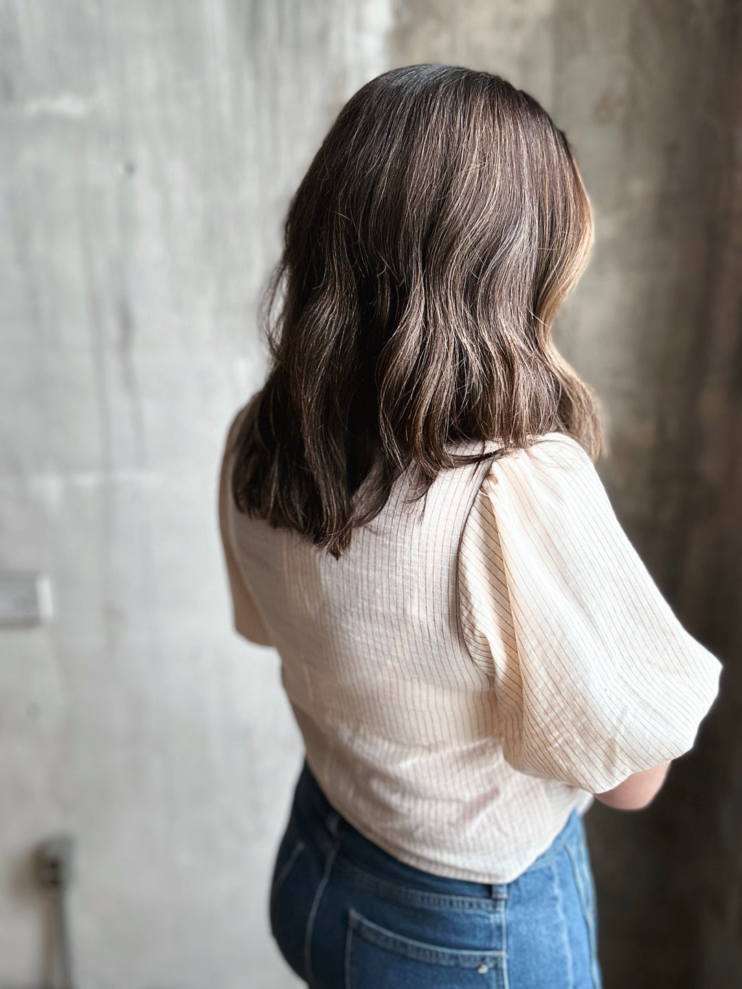 Person wearing a beige blouse and blue jeans against a textured wall.