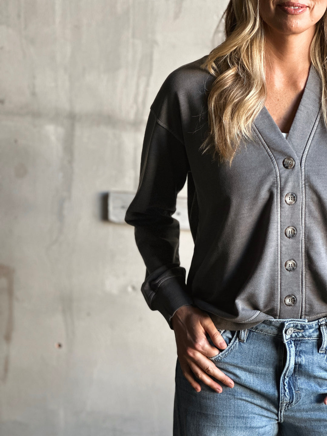 Person wearing a black and gray button-up shirt with jeans against a concrete wall.