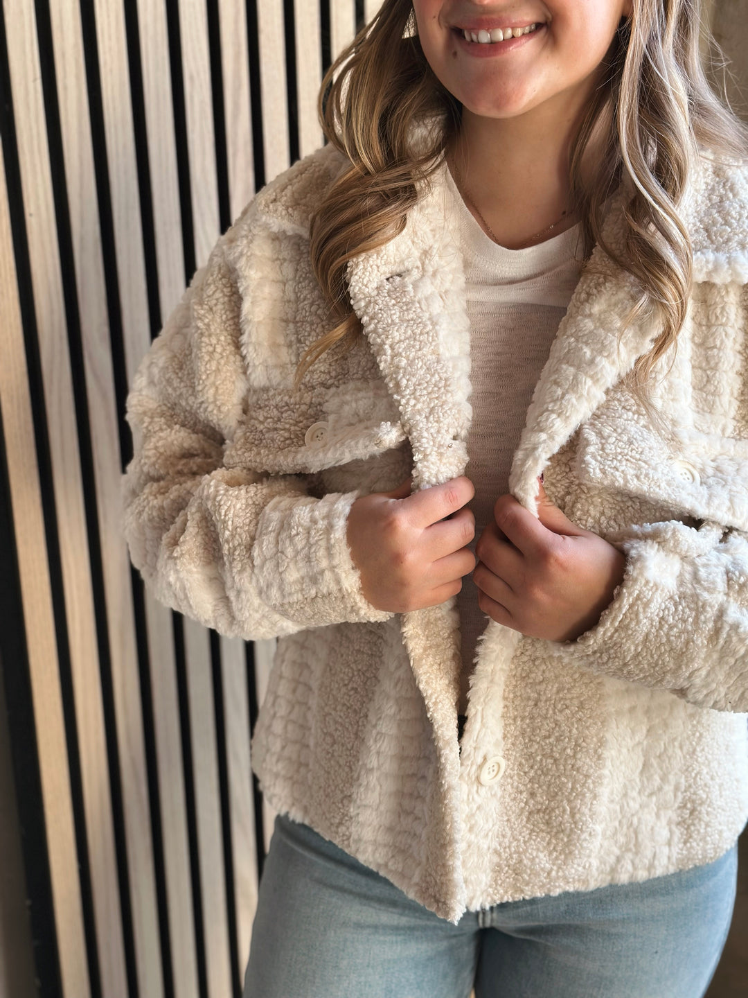 Person wearing a beige sherpa jacket with a neutral background