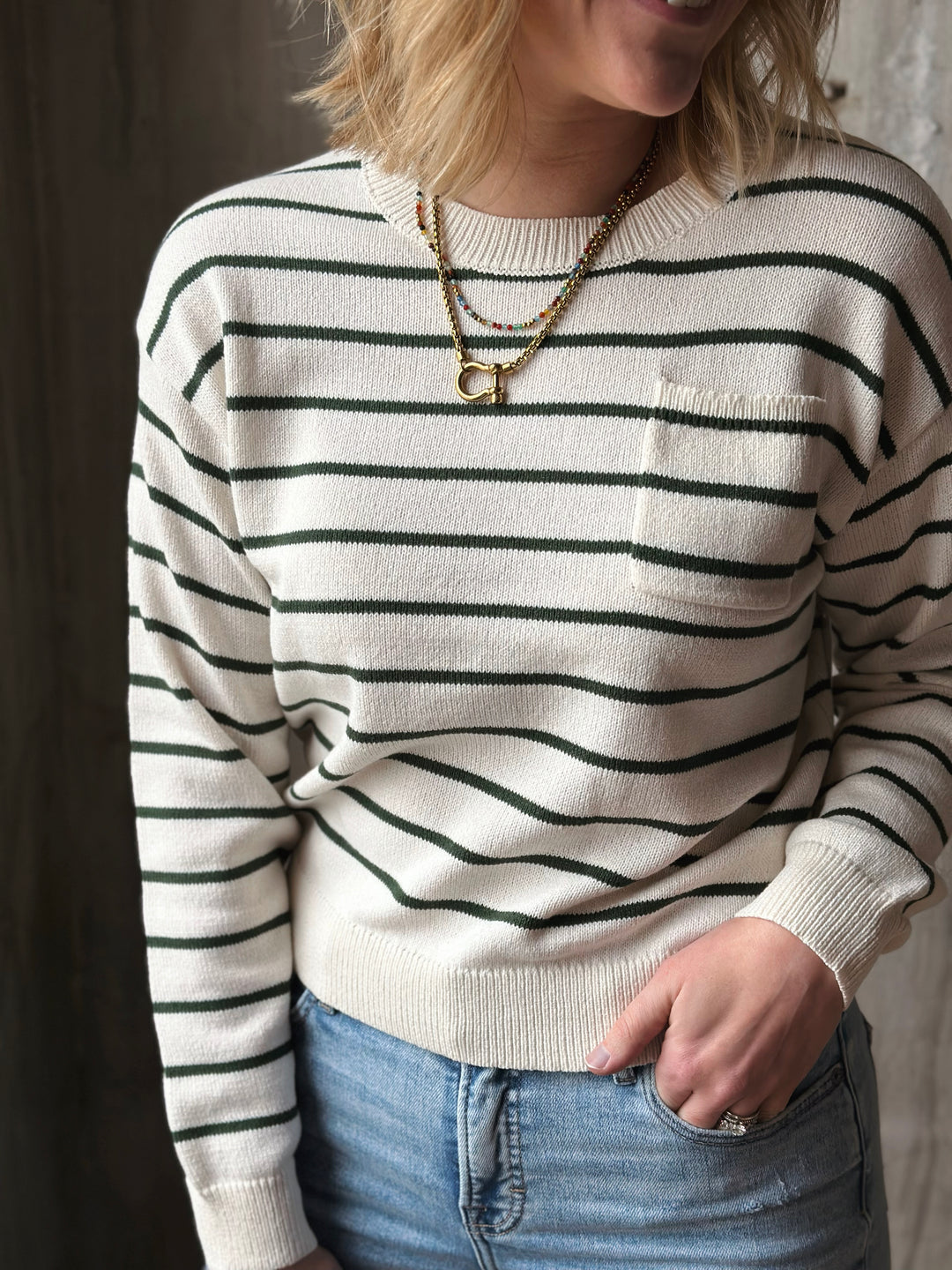 Person wearing a white sweater with black stripes and blue jeans, standing against a neutral background.