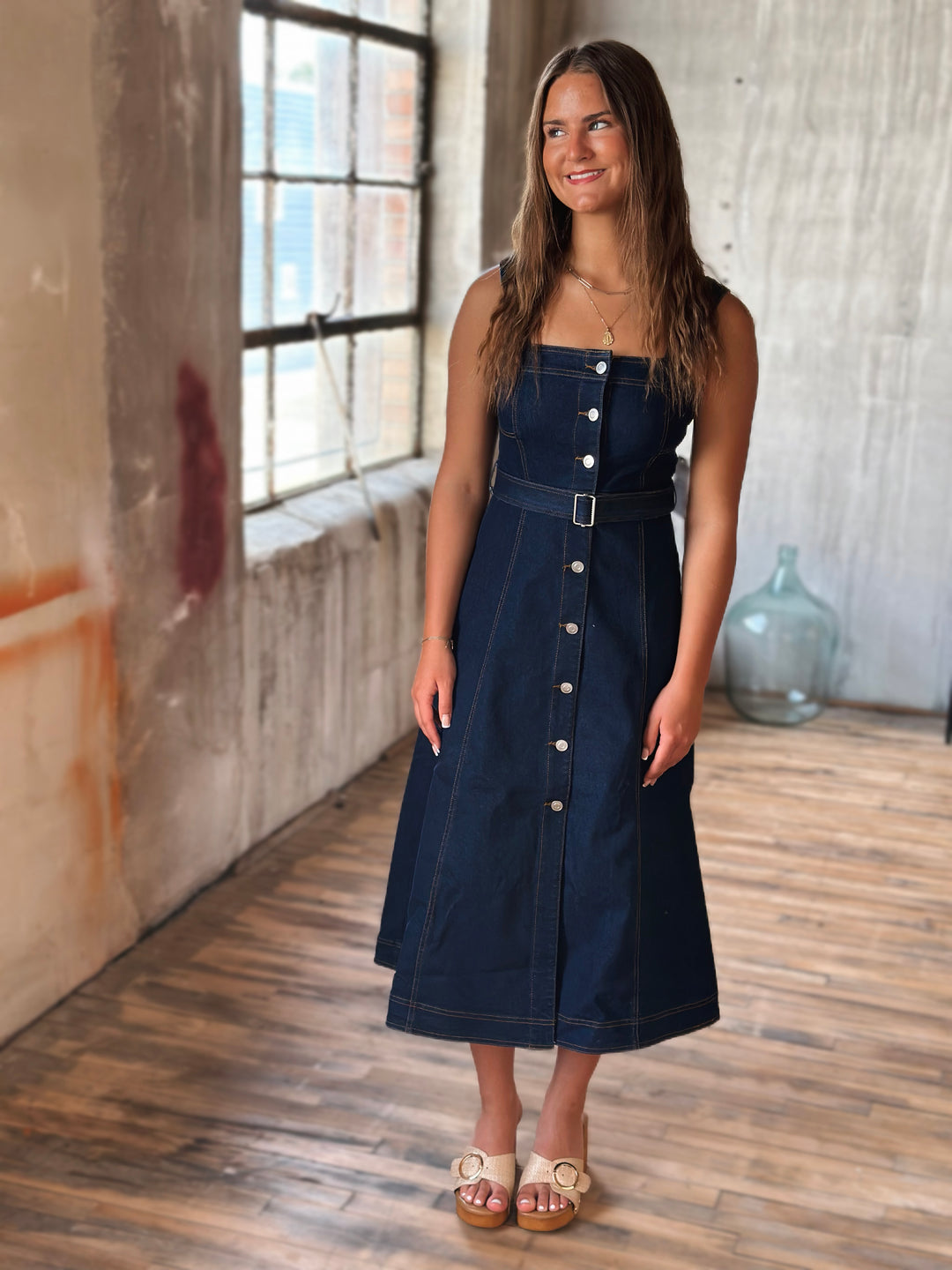 Woman wearing a dark blue denim dress with silver buttons in an indoor setting.