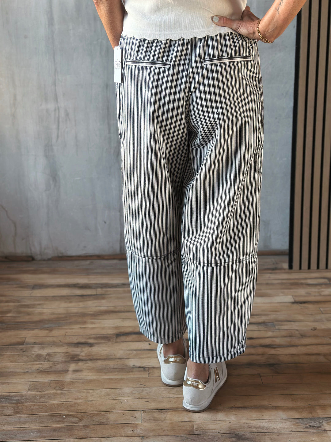 Person wearing black and white striped pants on a wooden floor with a gray wall background