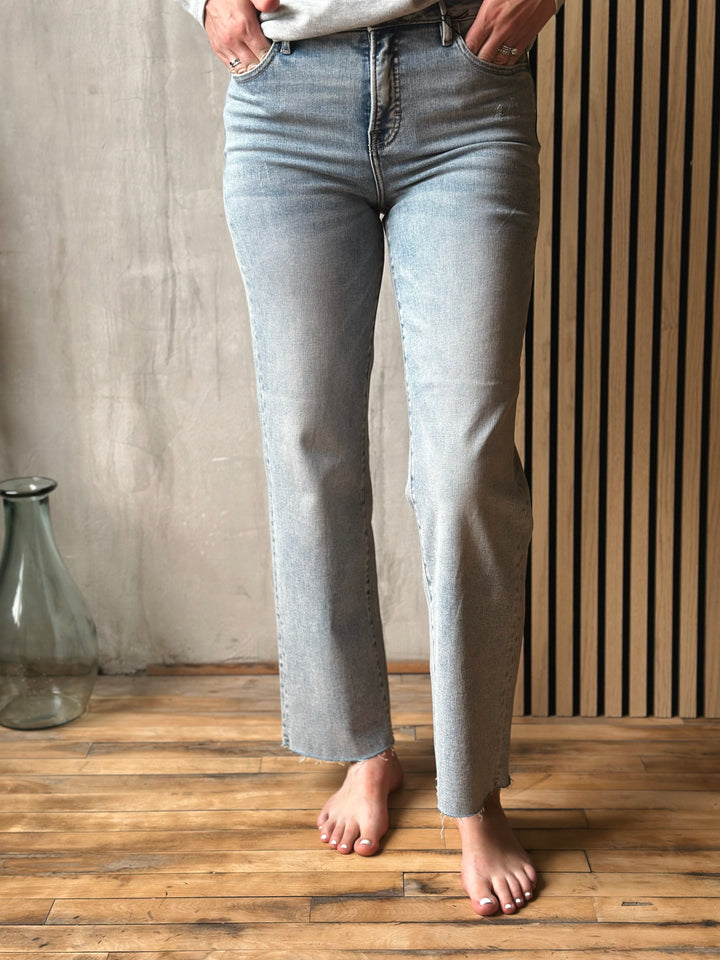 Person wearing light blue jeans standing on a wooden floor with a neutral background