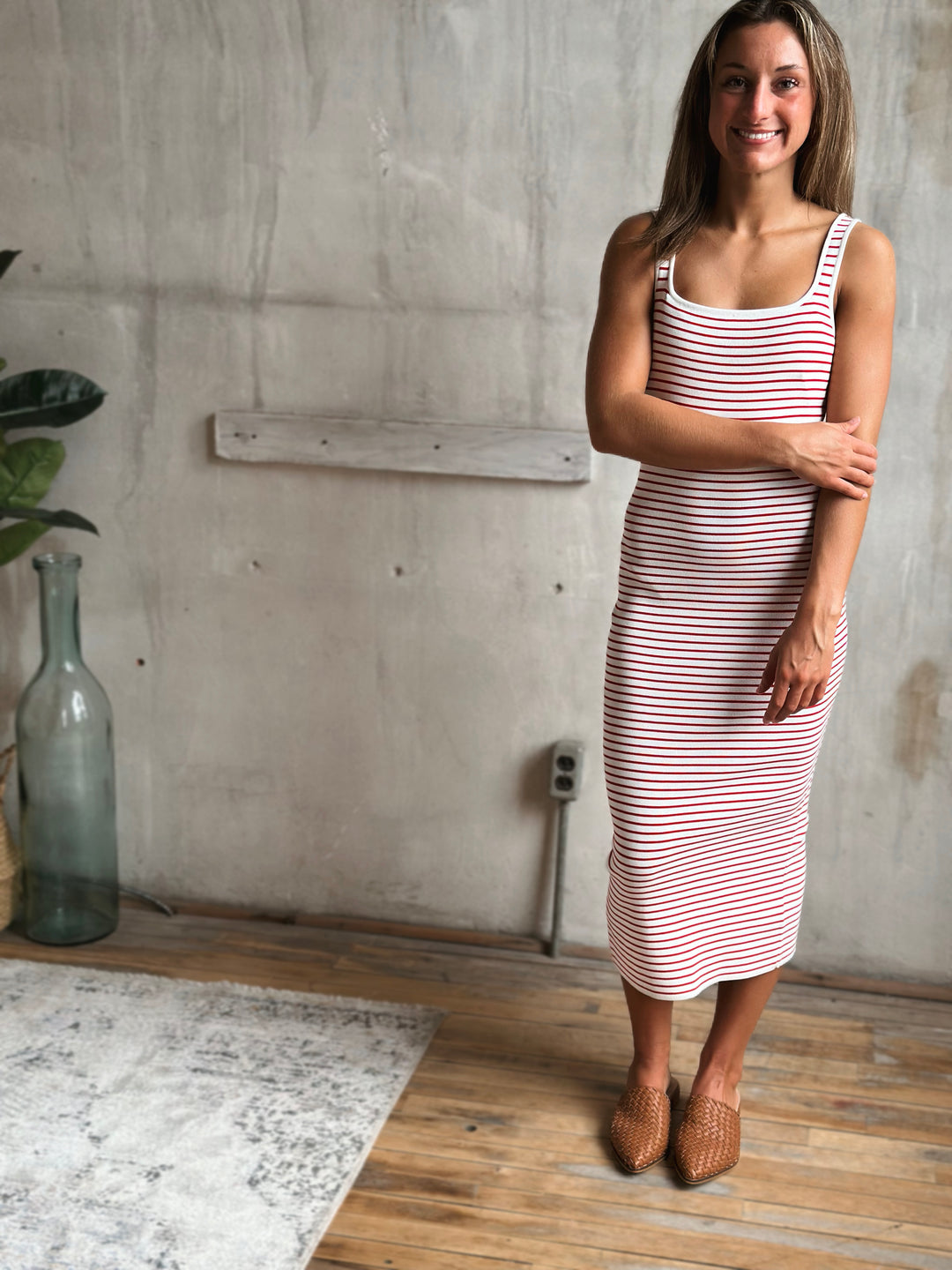 Woman wearing a red and white striped dress standing in a room with a concrete wall and wooden floor.