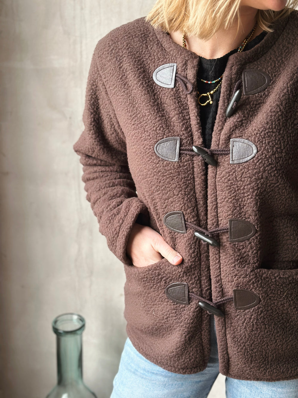 Person wearing a brown duffle coat with visible buttons against a neutral background