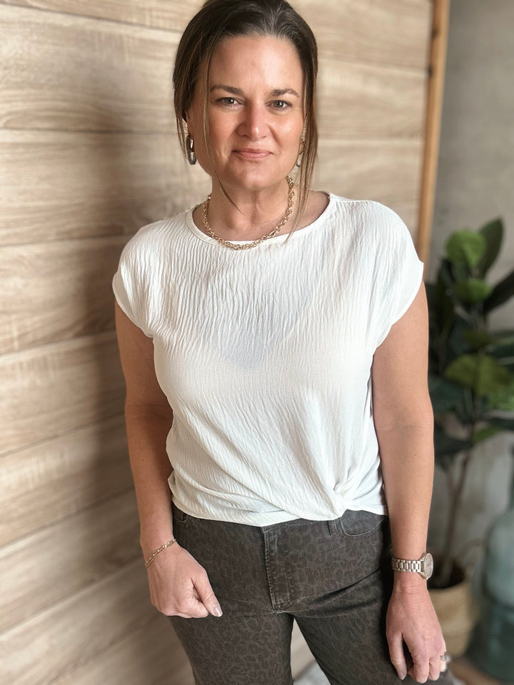 Woman wearing a white blouse and dark pants against a wooden wall.