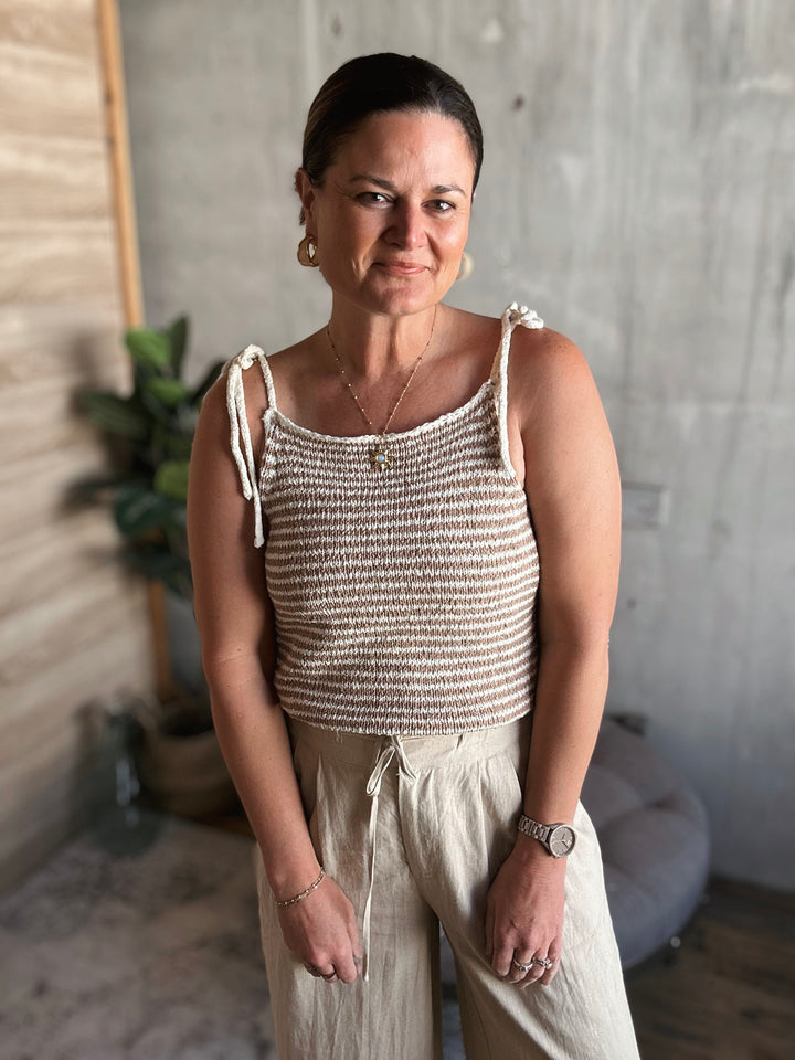Woman wearing a beige knitted tank top and light-colored pants indoors.