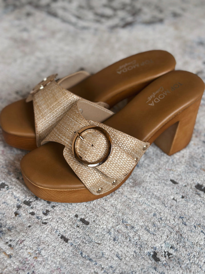 Pair of gold sandals with wooden sole on a textured surface.